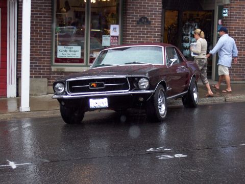 1972 Ford Ranchero - A 1967 Ford Mustang is parked on a wet street, with two people walking past the storefront.
