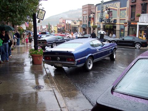 1972 Ford Ranchero - A blue 1971 Ford Mustang Mach 1 is parked on a wet street in front of shops.