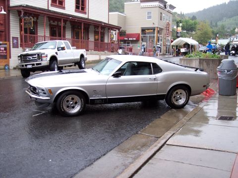 1972 Ford Ranchero - A classic Mustang Mach 1 is parked on a wet street in a town with shops and buildings.