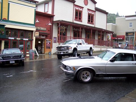 1972 Ford Ranchero - A silver 1969 Ford Mustang Mach 1 is parked on a wet street in front of buildings.