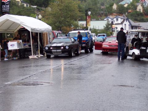 1972 Ford Ranchero - Several vehicles are parked on a wet street near a tent and buildings.