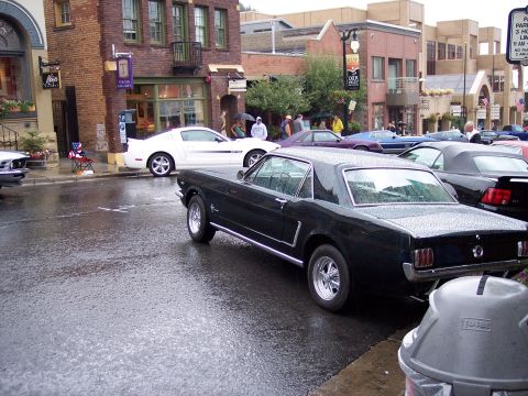 1972 Ford Ranchero - A black 1965 Ford Mustang coupe is parked on a wet street, with other vehicles visible in the background.