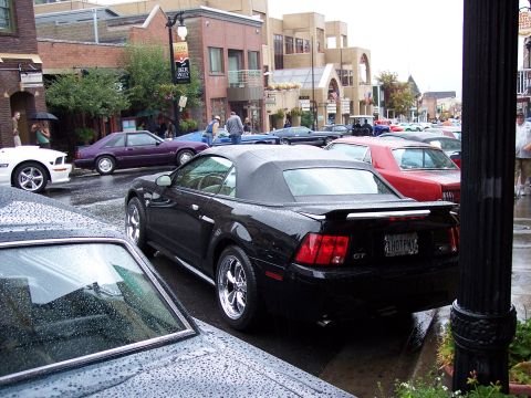 1972 Ford Ranchero - A black 2000 Ford Mustang GT convertible is parked on a wet street with other vehicles.