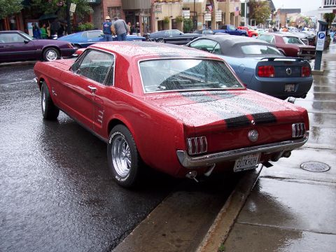 1972 Ford Ranchero - A classic red coupe with racing stripes sits on a wet street, reflecting the overcast sky.