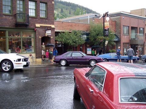 1972 Ford Ranchero - Several cars are parked on a wet street in front of brick buildings.