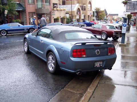 1972 Ford Ranchero - A blue convertible Mustang is parked on a wet street, with other vehicles visible in the background.