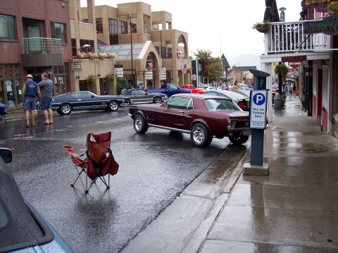 1972 Ford Ranchero - Maroon 1967 Ford Mustang coupe parked on a wet street with a parking meter nearby.