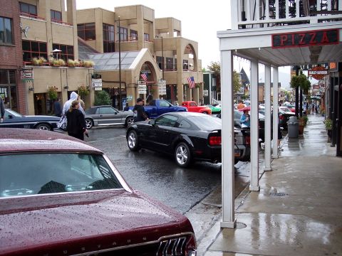 1972 Ford Ranchero - A black Ford Mustang is parked on a wet street in front of shops.