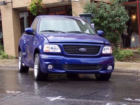1972 Ford Ranchero - A blue Ford F-150 SVT Lightning pickup truck is parked on a wet street.