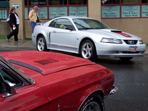 1972 Ford Ranchero - Two Ford Mustangs, one modern and one classic, are parked on a wet street.