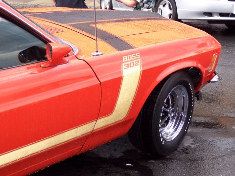 1972 Ford Ranchero - A red car with distinctive racing stripes and a BOSS 302 emblem is parked on a wet surface.