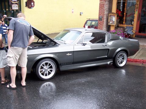 1972 Ford Ranchero - A classic gray Shelby GT500 is displayed with its hood up on a wet street in front of a building.