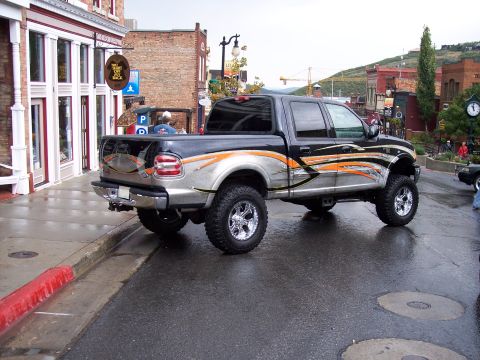 1972 Ford Ranchero - Lifted pickup truck with custom graphics parked on a wet street in a town.