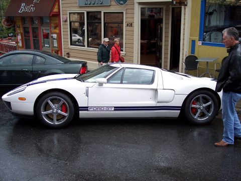 1972 Ford Ranchero - A white Ford GT is parked on a wet street in front of shops, with a man observing it.