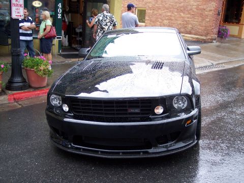 1972 Ford Ranchero - A black Ford Mustang is parked on a wet street, reflecting the overcast sky.