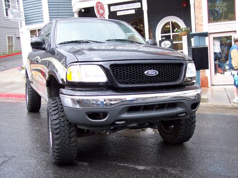 1972 Ford Ranchero - Lifted black Ford F-150 pickup truck parked on a wet street in front of a building.