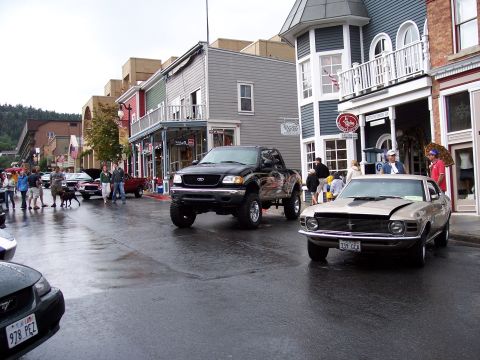 1972 Ford Ranchero - A tan 1969 Ford Mustang is parked on a wet street in front of shops.
