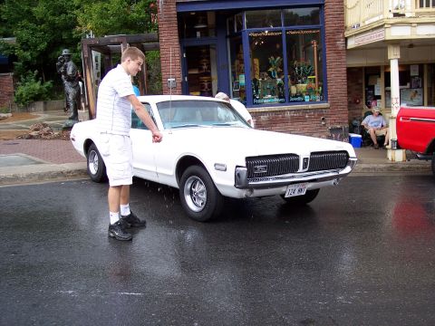 1972 Ford Ranchero - A white 1969 Mercury Cougar is parked on a wet street, with a young man standing by the open driver's door.