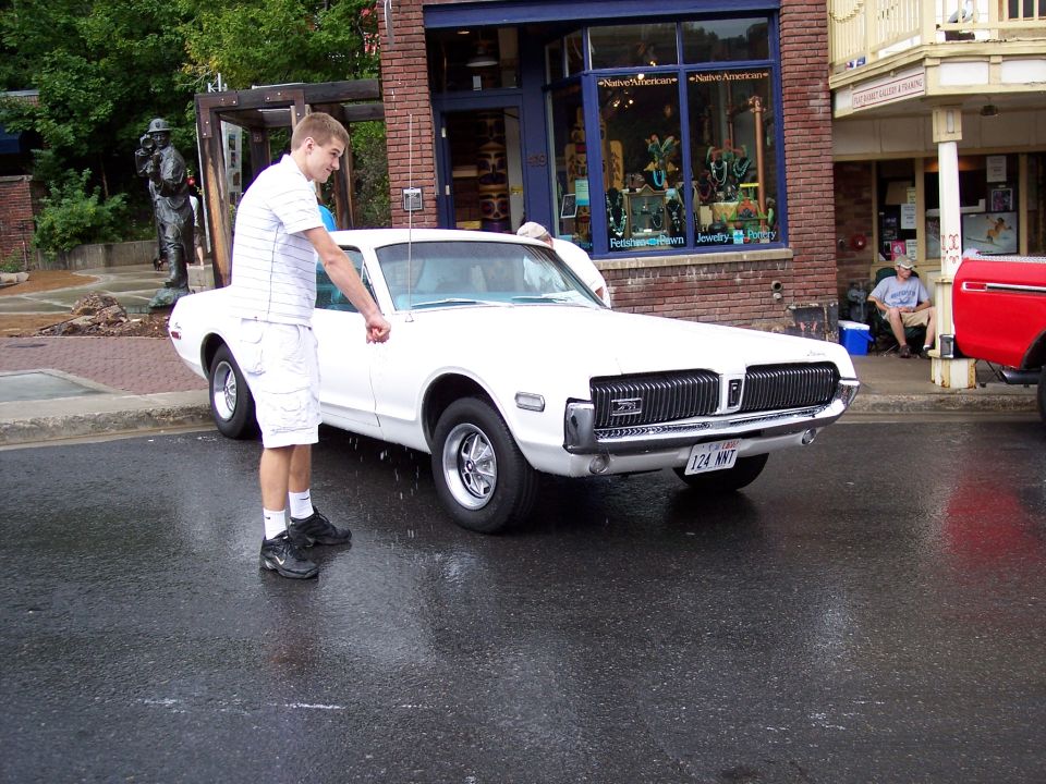 White vintage coupe on wet street with man standing beside it near brick storefront