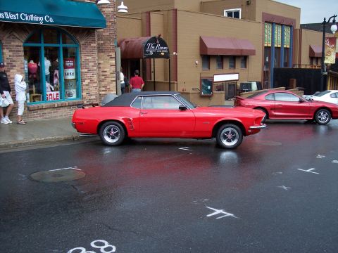 1972 Ford Ranchero - A classic red convertible is parked on a wet street in front of shops and a restaurant.
