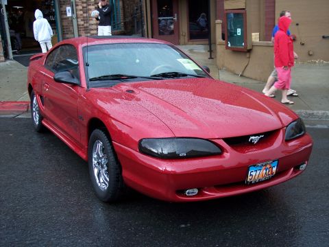 1972 Ford Ranchero - A red 1994 Ford Mustang is parked on a wet street in front of a building.