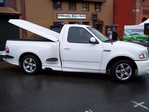1972 Ford Ranchero - A white pickup truck is parked on a wet street in front of a restaurant.