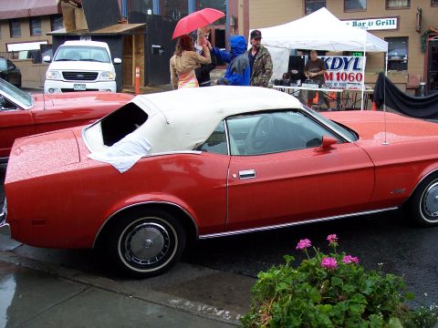 Red convertible with white top, side view, in wet parking lot at car show