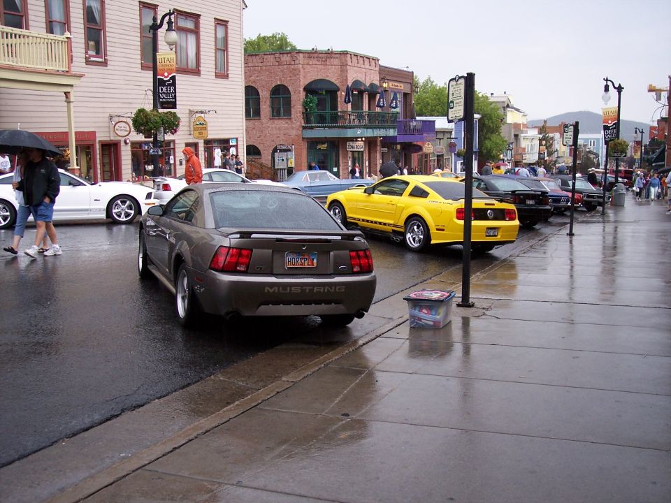Gray Ford Mustang coupe parked on a wet street at a car show, rear 3/4 view