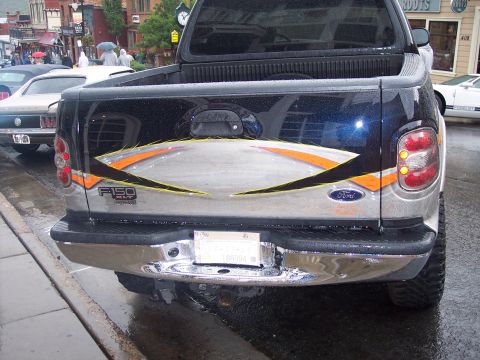 Rear of black Ford F-150 pickup with custom tailgate graphics, parked on wet street.