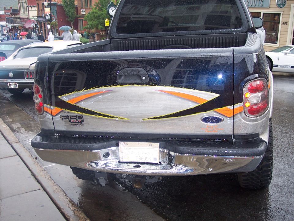 Rear of black Ford F-150 pickup with custom tailgate graphics, parked on wet street.
