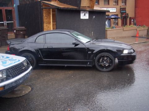 Black Mustang GT coupe in side view on wet street with white flamed car in foreground