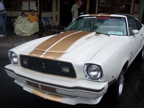 White Mustang II Cobra II with gold stripes, front 3/4 view at a car show