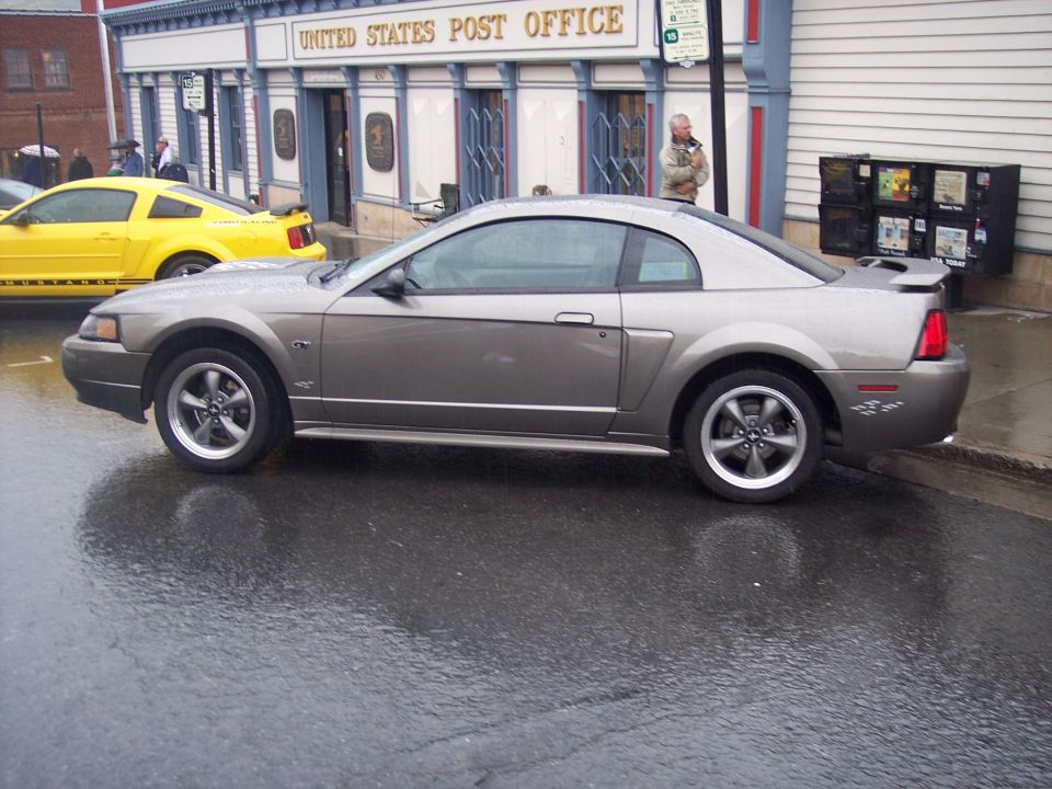 Gray Ford Mustang coupe parked in profile on wet street outside a post office