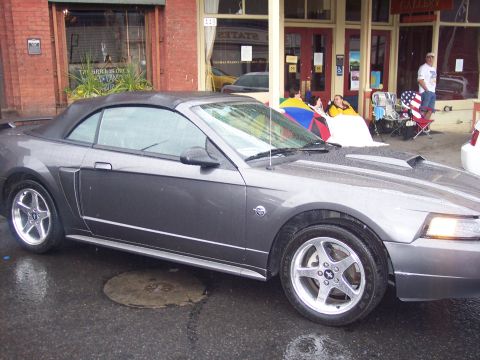 Gray Ford Mustang convertible, top up, parked in profile on wet street
