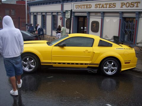 Yellow Ford Mustang coupe parked in front of a US Post Office on a wet street
