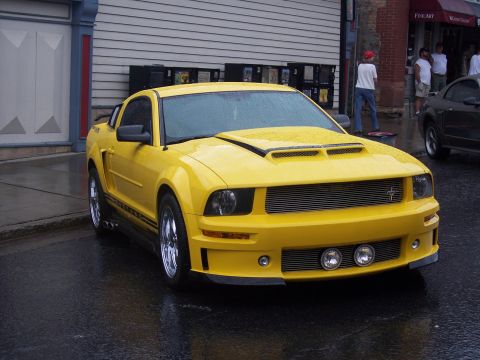 Yellow Ford Mustang coupe with black stripes parked on wet street, 3/4 front view