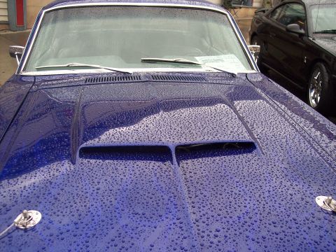 Rain-covered dark blue car hood with hood scoop and windshield wipers