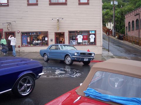 Light blue vintage Mustang coupe on wet street with other classic cars in foreground