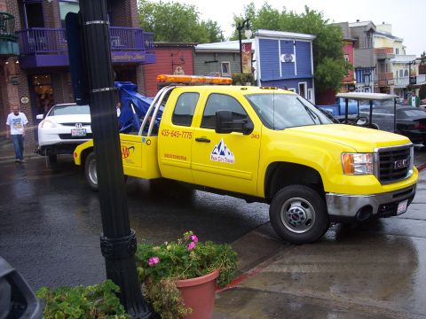 Yellow GMC tow truck with orange light bar parked on a wet city street.