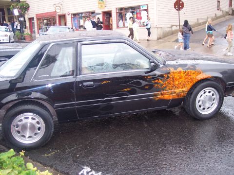 Black coupe with orange flame graphics, side view on wet street