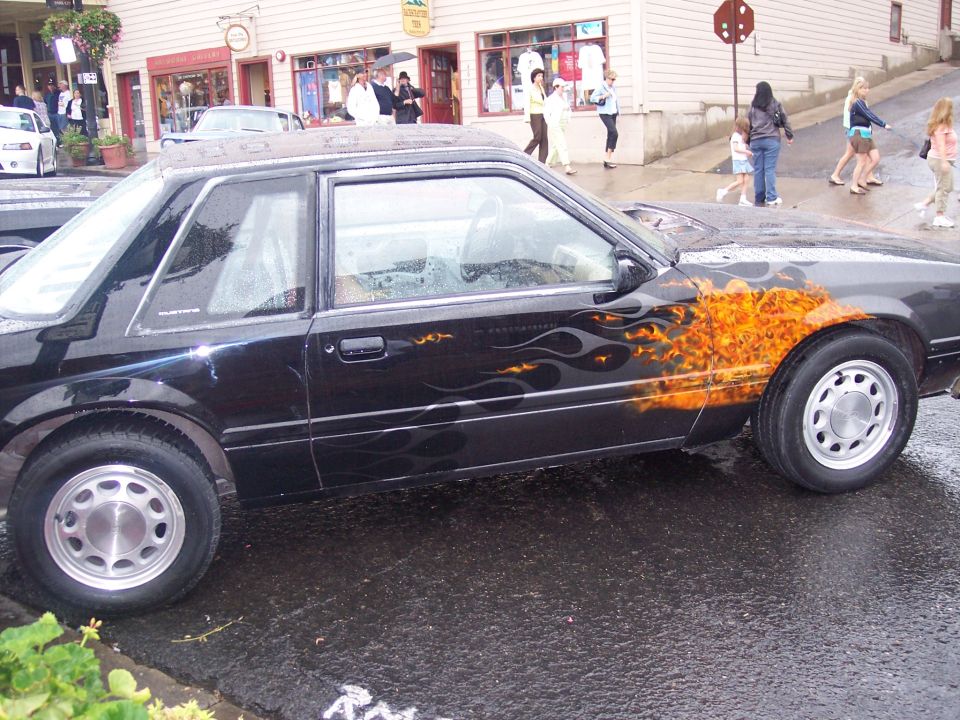 Black coupe with orange flame graphics, side view on wet street