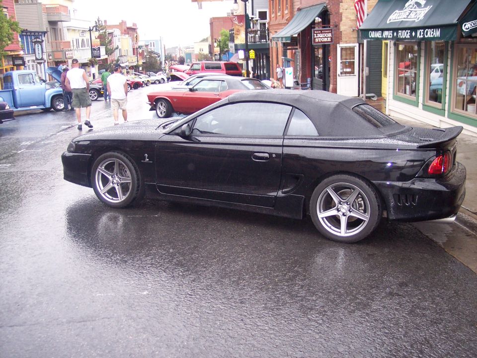 Black convertible coupe with chrome wheels parked on a wet street at a car show
