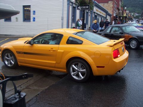 Orange Ford Mustang GT/CS coupe, rear 3/4 view, parked on wet street