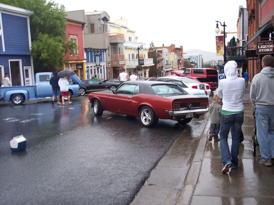 Maroon classic Mustang coupe parked on wet street at a car show