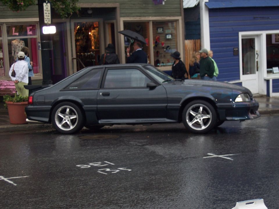 Charcoal Fox-body Mustang hatchback in side view on a wet street