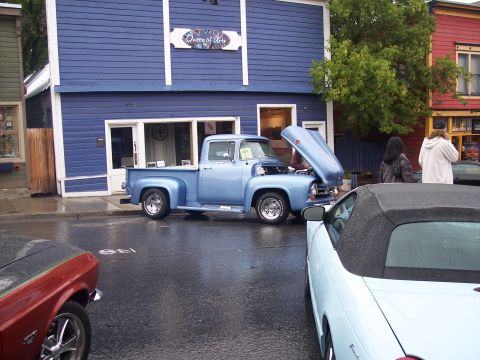Light blue classic Ford pickup with open hood parked on wet street at car show