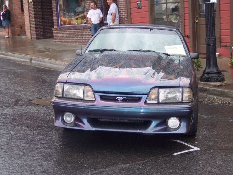 Fox-body Ford Mustang GT in purple-teal color-shift paint parked on a wet street, front view