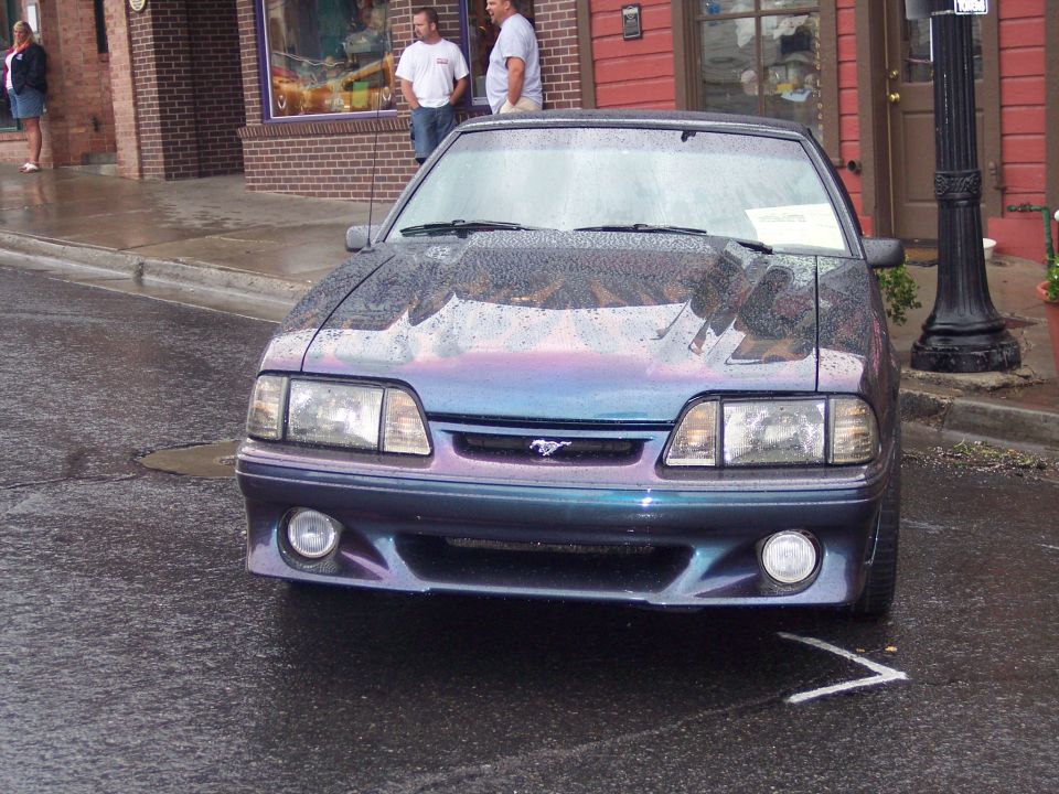 Fox-body Ford Mustang GT in purple-teal color-shift paint parked on a wet street, front view