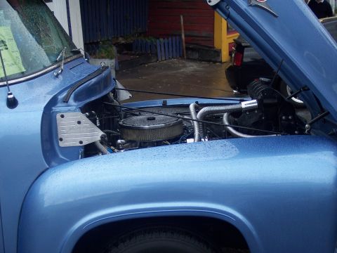 Engine bay of a blue vehicle with round chrome air cleaner and open hood