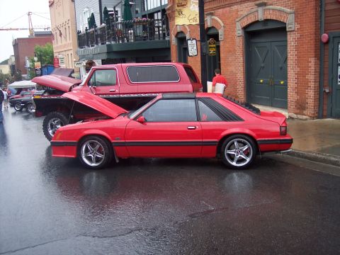 Red Fox-body Mustang hatchback parked in profile on a wet street at a car show